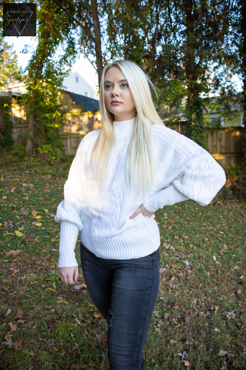 Women's white cable knit sweater, high mock neckline, long balloon sleeves with exaggerated ribbed cuffs, and a relaxed and flattering silhouette,